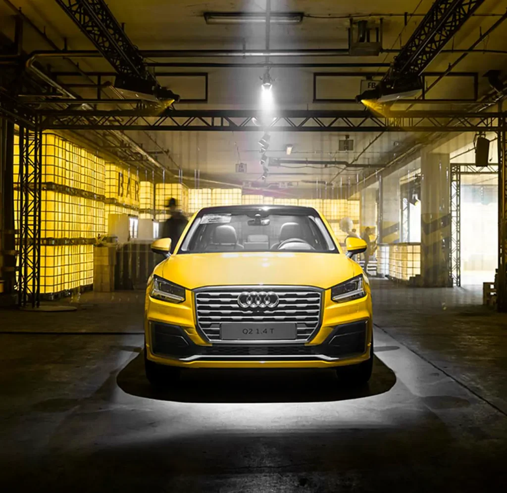 Audi Q2 amarillo bajo un foco cenital en una nave con estructura de truss