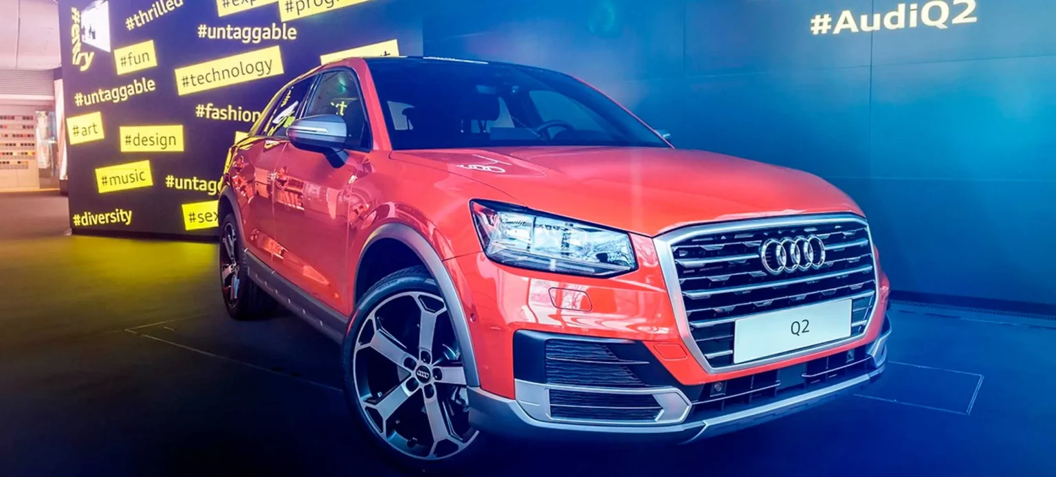 Audi Q2 naranja expuesto ante un fondo azul con la etiqueta #AudiQ2