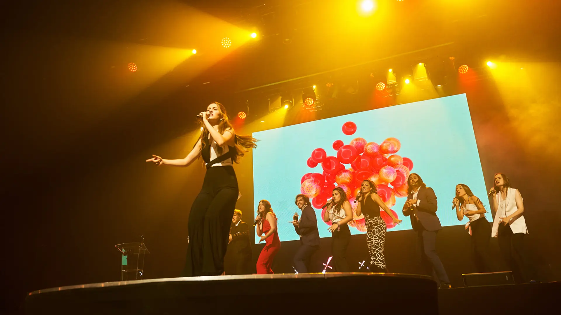 Cantante actuando en un escenario iluminado con focos amarillos ante una pantalla LED durante una gala de premios