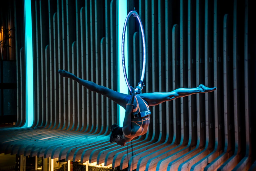 Acróbata haciendo un split en el aro aéreo ante una pared de luz azul