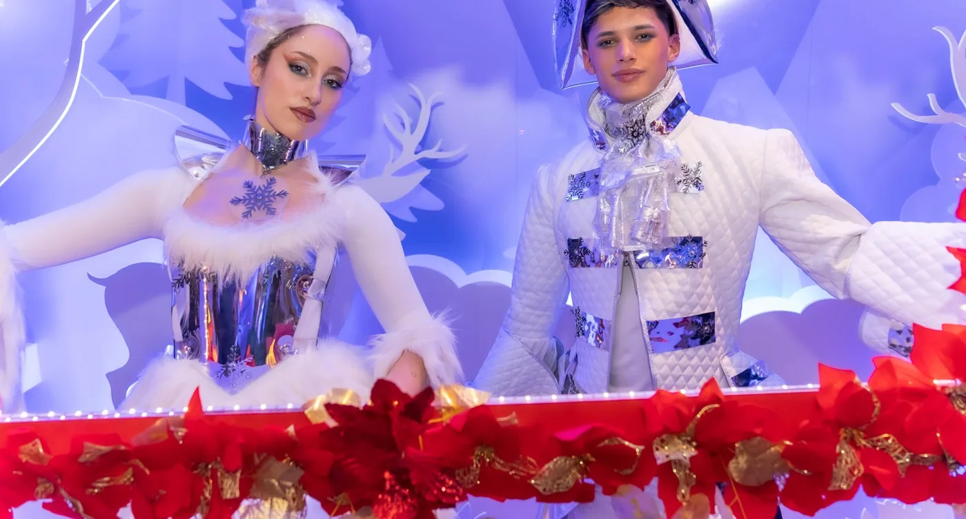 Pareja de artistas con vestuario de invierno dentro de un photocall de nieve y flores rojas