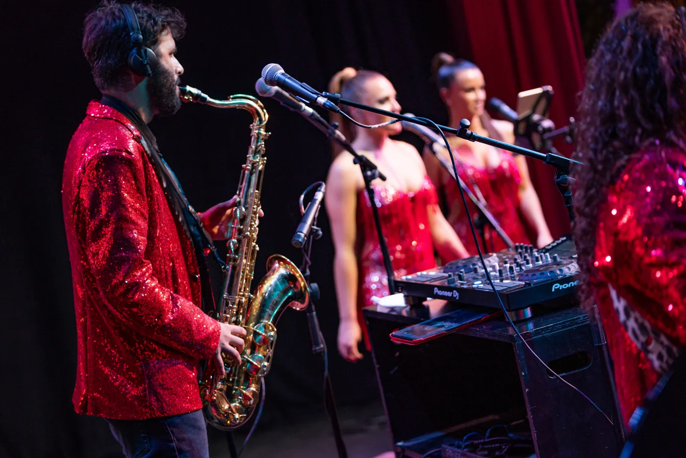 Saxofonista y cantantes con vestidos rojos actuando en directo en una fiesta de empresa