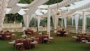 Carpa exterior con telas blancas y lámparas de araña sobre un jardín, con mesas redondas vestidas y sillas preparadas antes de un evento