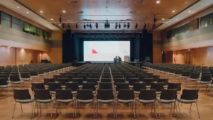 Sala de convenciones con filas de sillas vacías y técnicos preparando la pantalla LED del escenario antes de un evento de empresa