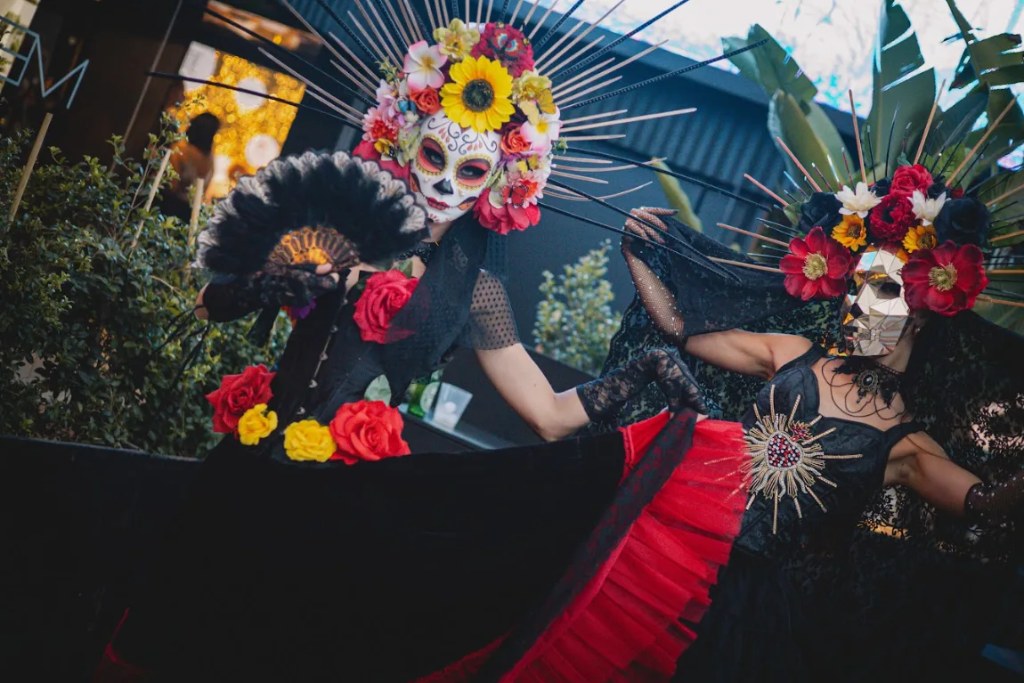 Dos catrinas con coronas de flores y abanico negro en un espectáculo del Día de Muertos
