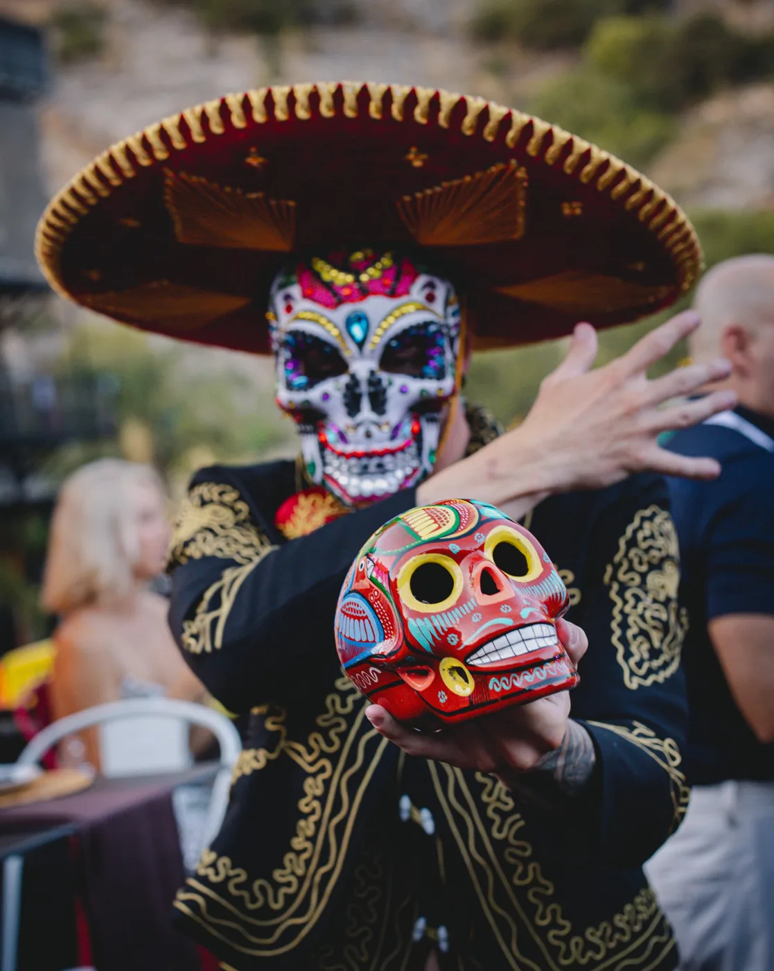 Mariachi con sombrero y máscara de calavera mostrando una calavera de colores