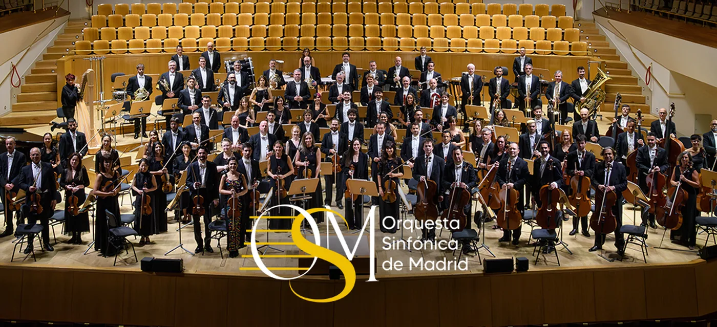 Los músicos de la Orquesta Sinfónica de Madrid posan con sus instrumentos en el escenario de una sala de conciertos, con el logotipo de la OSM