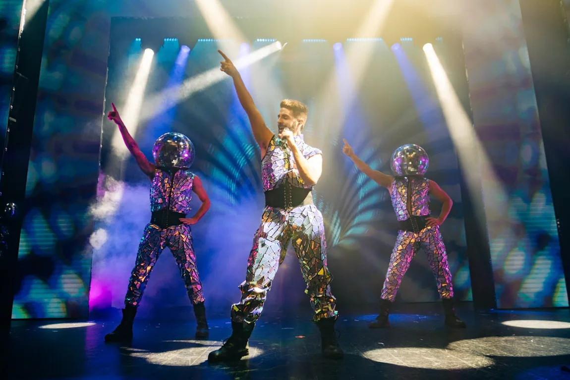 Cantante y bailarines con trajes de espejos y cascos de bola de discoteca en el escenario