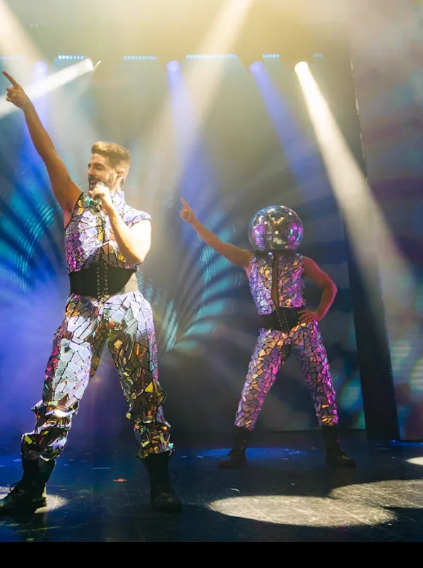 Cantante con traje de espejos señalando al cielo entre haces de luz en una fiesta disco