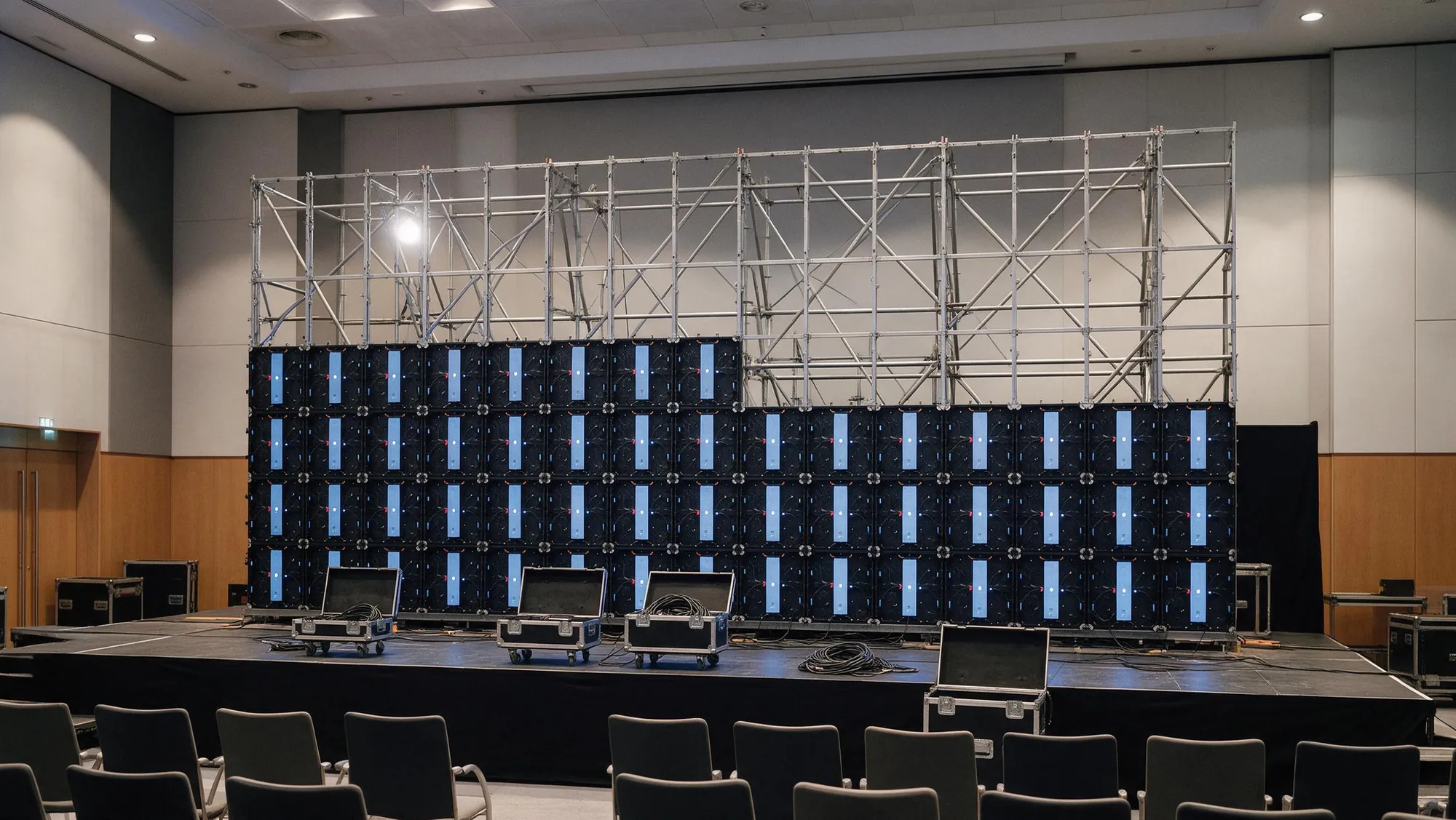 Pantalla LED a medio montar sobre el escenario de un auditorio vacío, con la estructura de truss a la vista y flight cases abiertos
