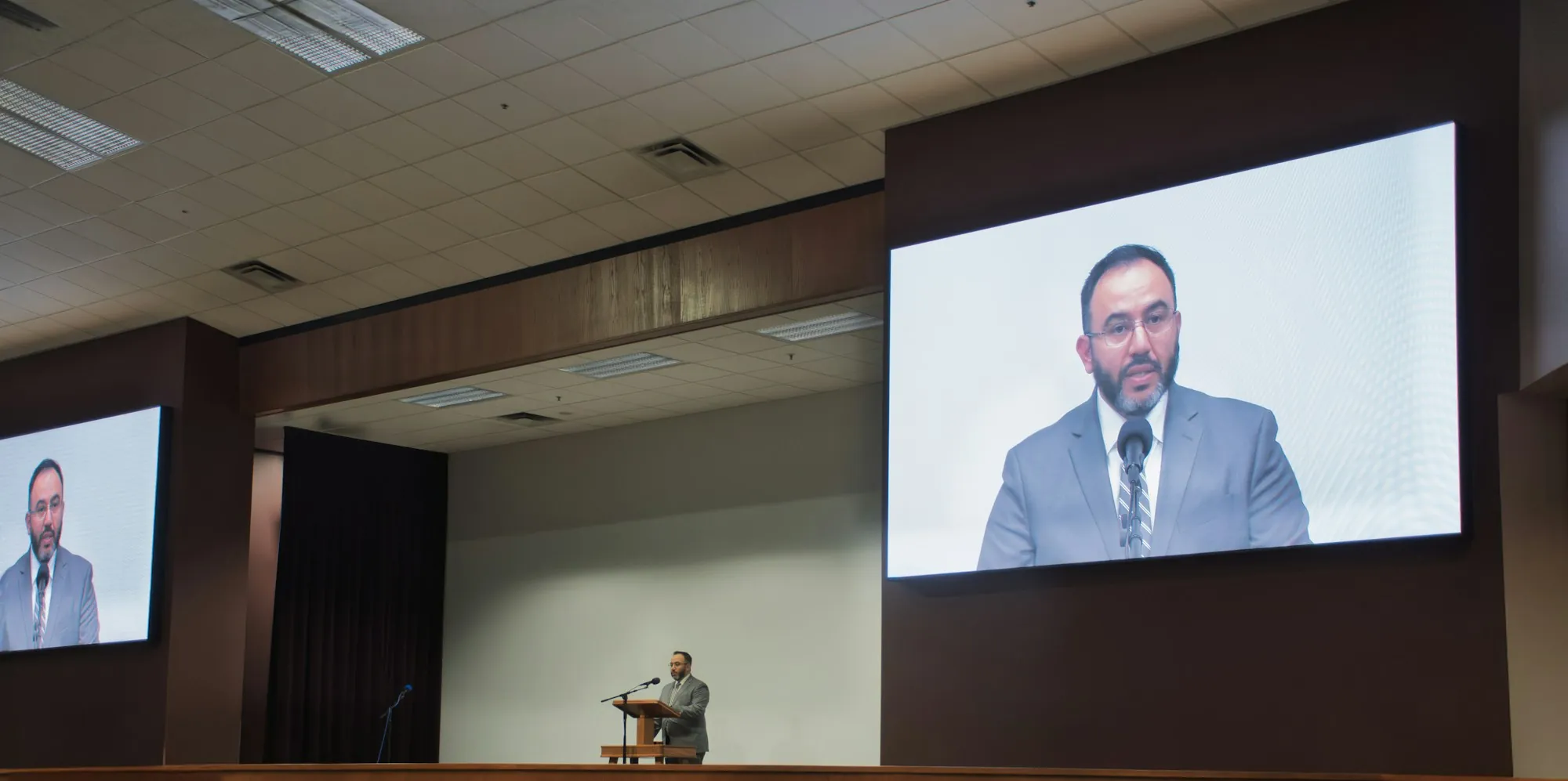 Ponente en un atril y dos pantallas LED laterales que muestran su imagen en una conferencia de empresa