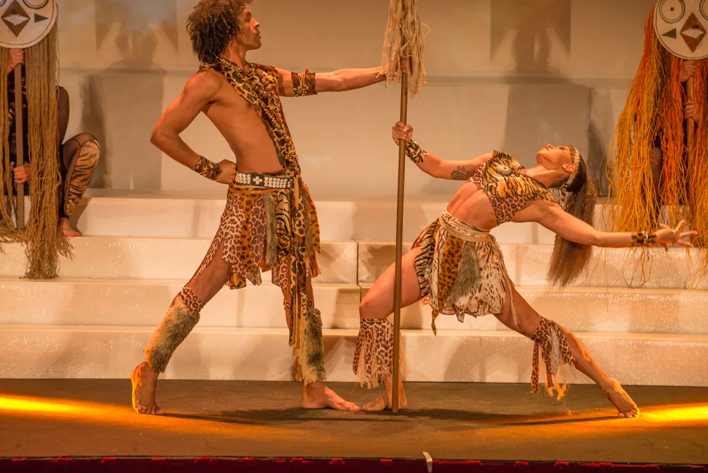 Pareja de bailarines con vestuario tribal de rafia en un número de danza sobre el escenario
