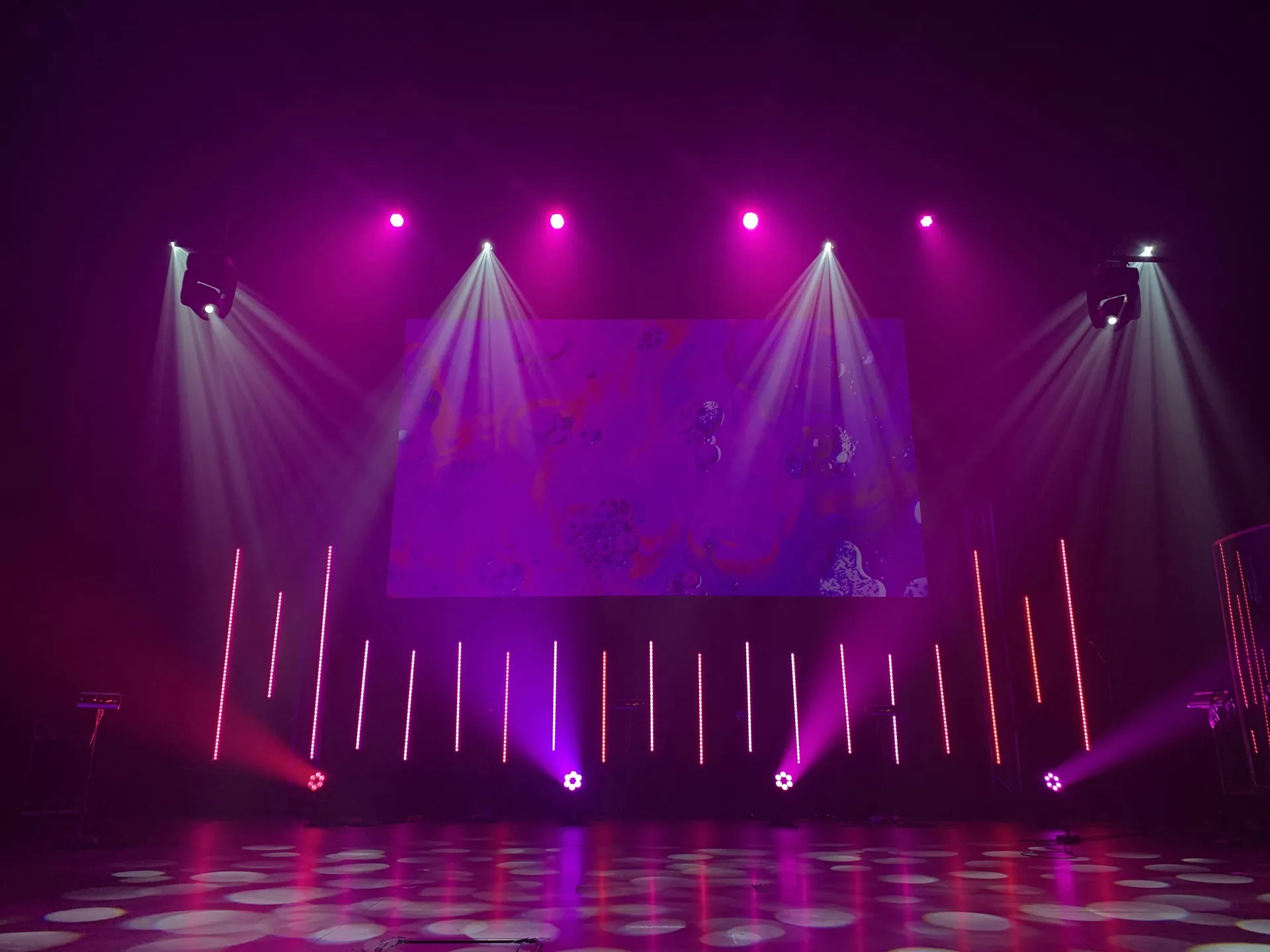 Escenario vacío con pantalla de vídeo, cabezas móviles y barras LED encendidas en tonos morados durante las pruebas de iluminación