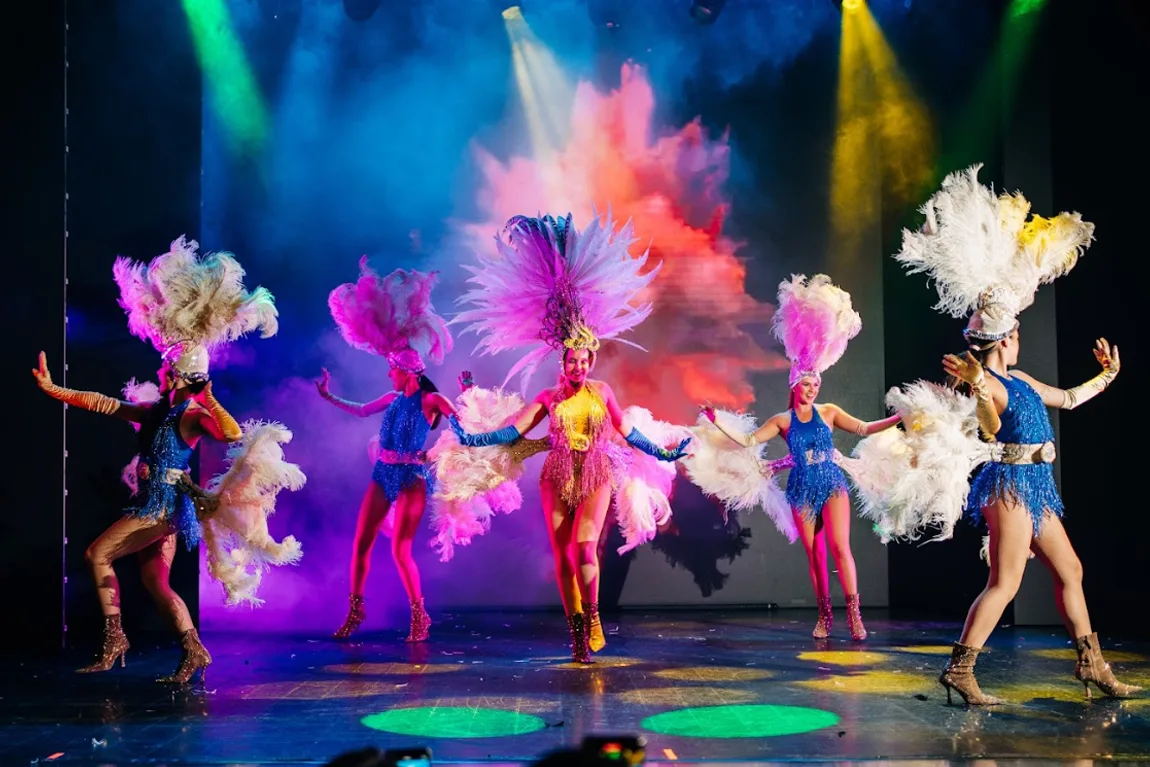 Bailarinas con tocados de plumas de colores en un show de música latina sobre el escenario