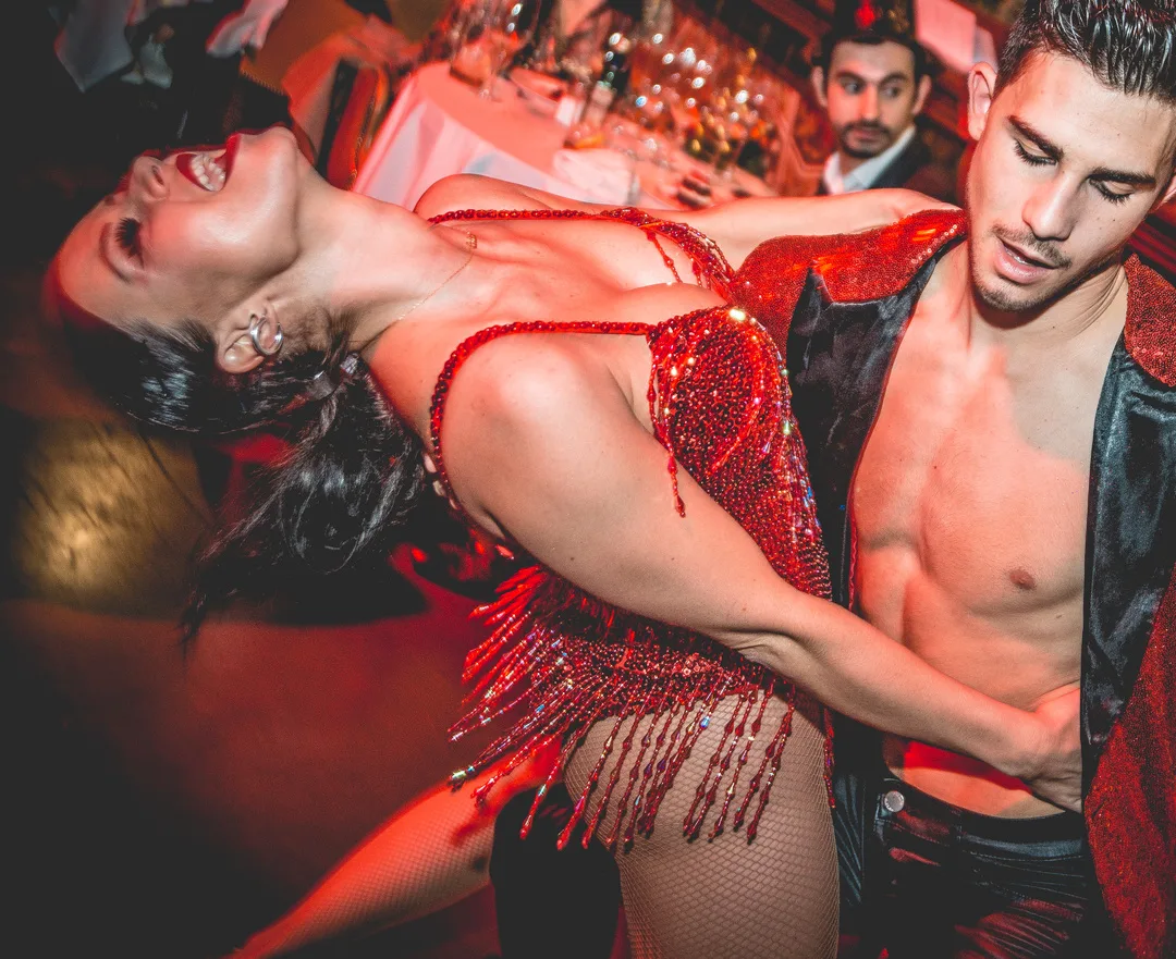 Pareja de baile latino con vestuario rojo de lentejuelas bailando entre las mesas