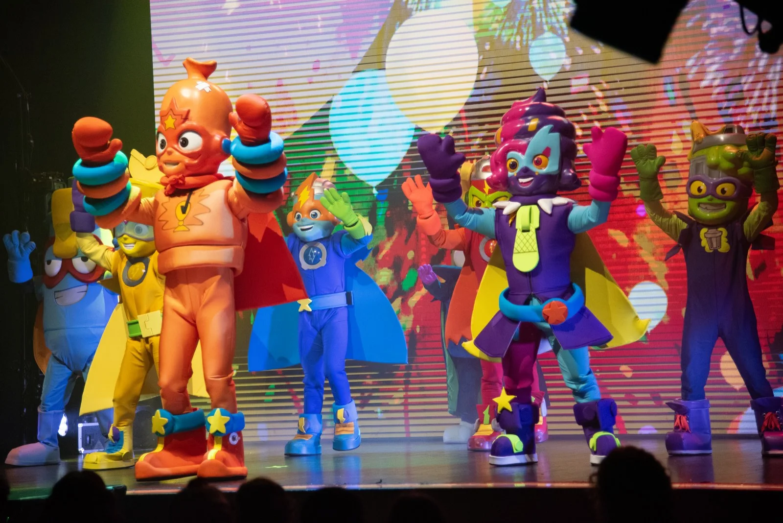 Personajes de SuperThings bailando en el escenario ante una pantalla con globos de colores