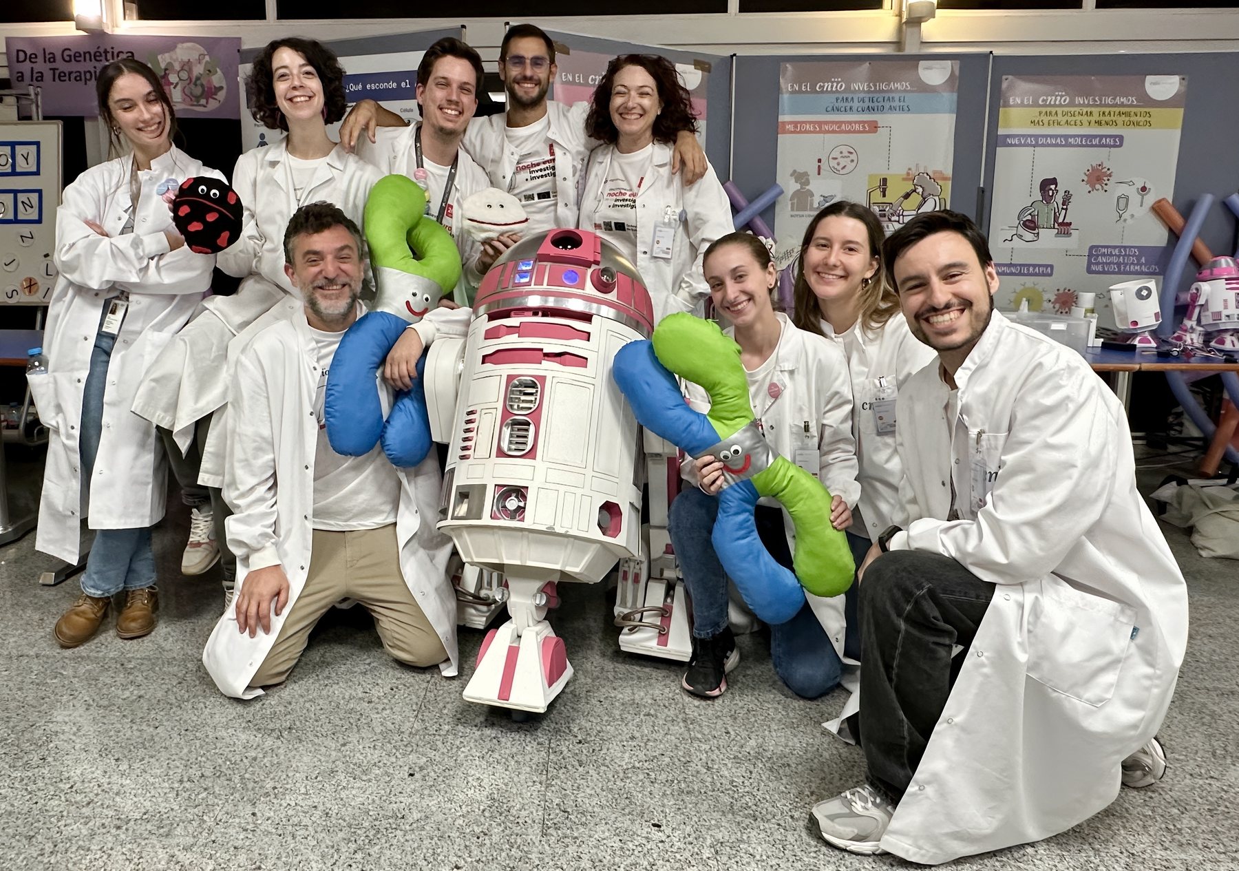 Equipo con batas blancas y peluches posando junto al droide rosa R2-KT