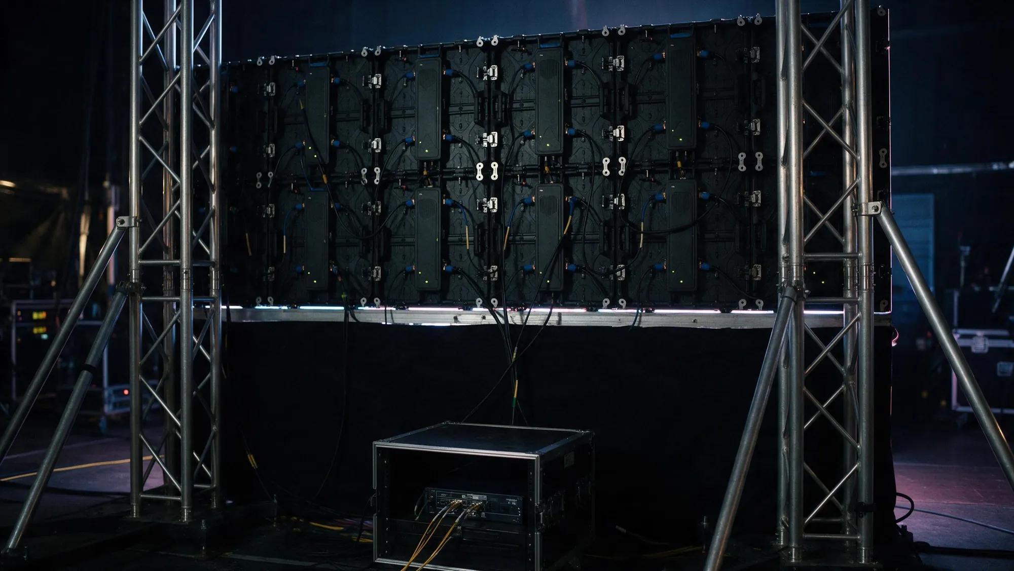 Parte trasera de una pantalla LED con los paneles unidos, el cableado de señal y corriente, torres de truss y el rack del procesador de vídeo